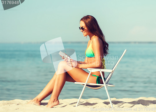 Image of smiling young woman sunbathing in lounge on beach