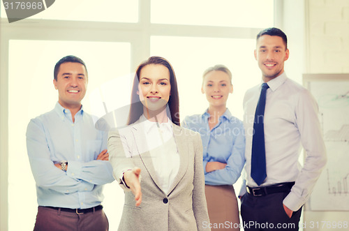 Image of smiling businesswoman in office with team on back