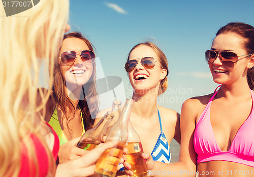 Image of group of smiling young women drinking on beach