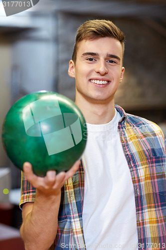 Image of happy young man holding ball in bowling club