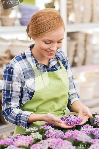 Image of happy woman taking care of flowers in greenhouse