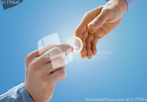 Image of close up of male gay couple hands giving condom