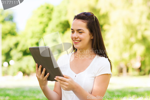 Image of smiling young girl with tablet pc sitting on grass