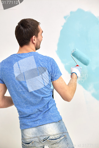 Image of man with roller painting wall in blue at home