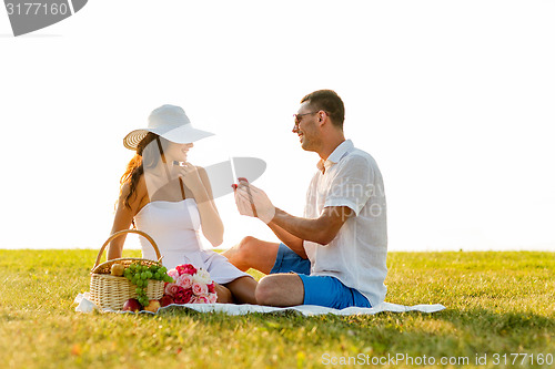 Image of smiling couple with small red gift box on picnic