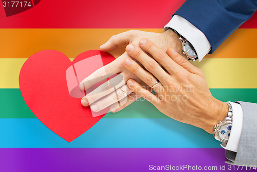 Image of close up of male gay couple hands with red heart