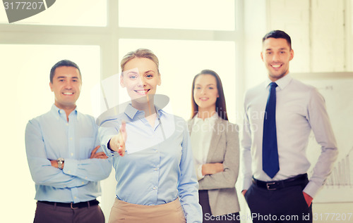 Image of smiling businesswoman in office with team on back