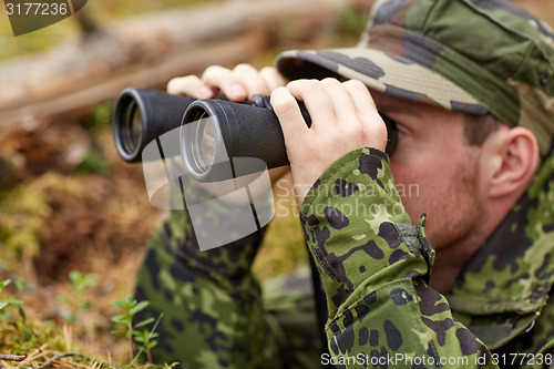 Image of young soldier or hunter with binocular in forest