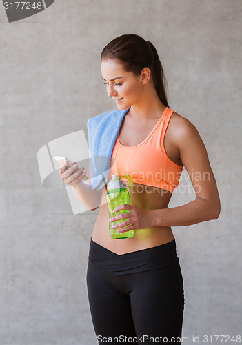 Image of woman with smartphone and bottle of water in gym