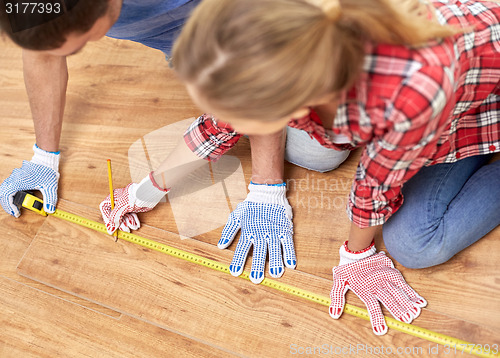 Image of happy couple with ruler measuring parquet board