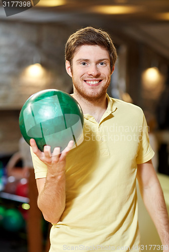 Image of happy young man holding ball in bowling club