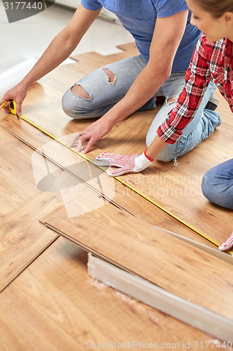 Image of happy couple with ruler measuring parquet board