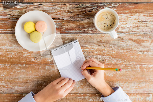 Image of close up of hands, notebook, coffee and cookies