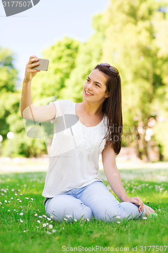 Image of smiling young girl with smartphone sitting in park