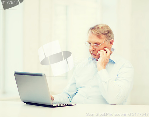 Image of old man in eyeglasses working with laptop at home