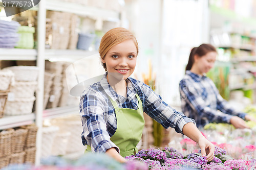 Image of happy woman taking care of flowers in greenhouse