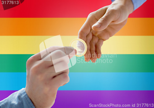 Image of close up of male gay couple hands giving condom