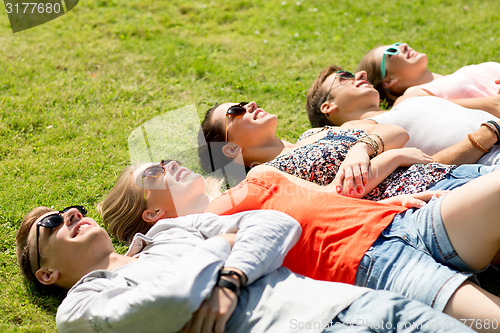 Image of group of smiling friends lying on grass outdoors