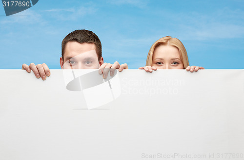 Image of happy couple hiding behind big white blank board