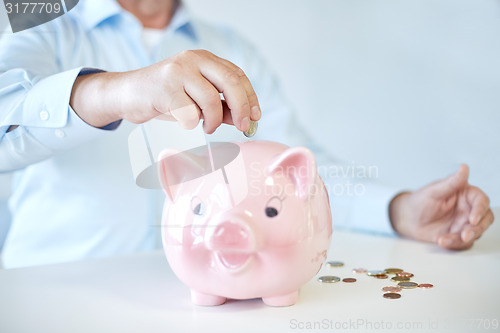 Image of close up of old man putting coins into piggybank