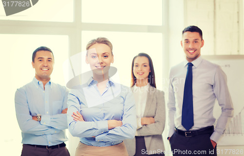 Image of smiling businesswoman in office with team on back