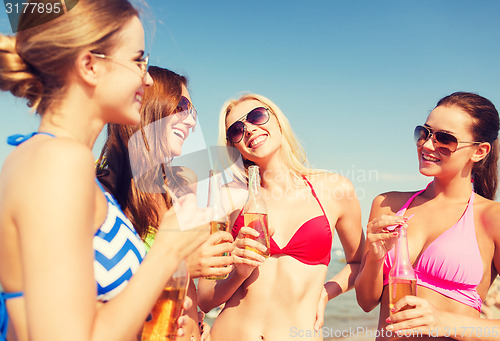 Image of group of smiling young women drinking on beach