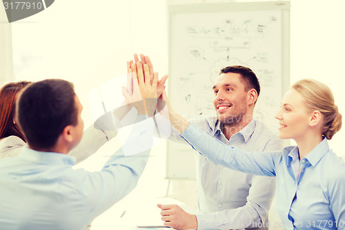 Image of happy business team giving high five in office