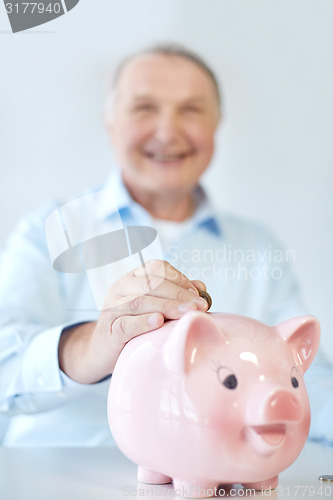 Image of close up of old man putting coin into piggybank