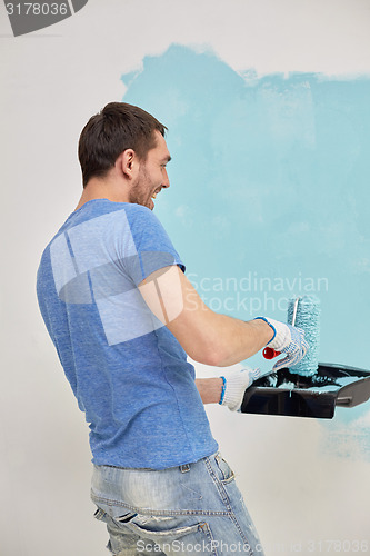 Image of happy man with roller painting wall at home