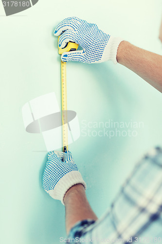 Image of closeup of male in gloves measuring wall with tape