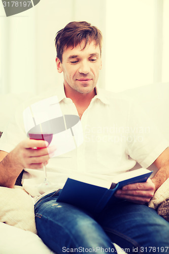 Image of happy man with book and glass of rose wine at home