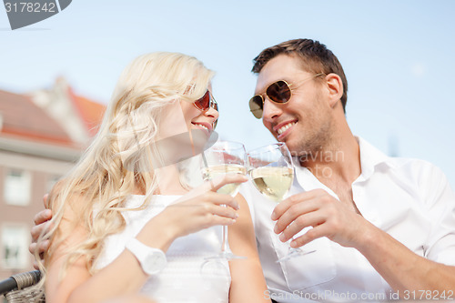 Image of smiling couple in sunglasses drinking wine in cafe