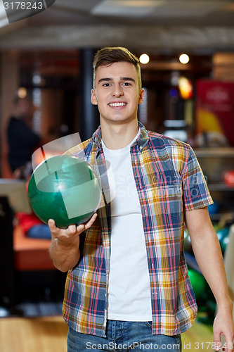 Image of happy young man holding ball in bowling club