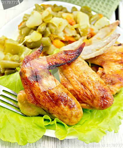 Image of Chicken wings fried with vegetables in plate on board