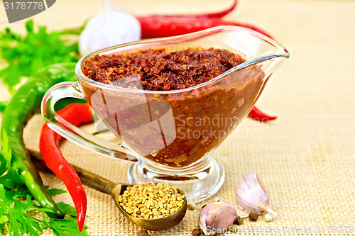 Image of Adjika in glass gravy boat with fenugreek on sacking