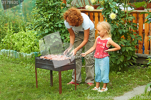 Image of Little girl helping her mother to cook shish kebab