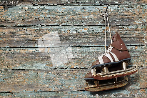 Image of vintage pair of  ice skates hanging on a cracked paint wall