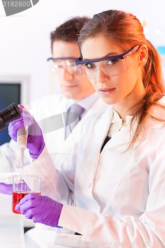 Image of Young scientist pipetting red solution.