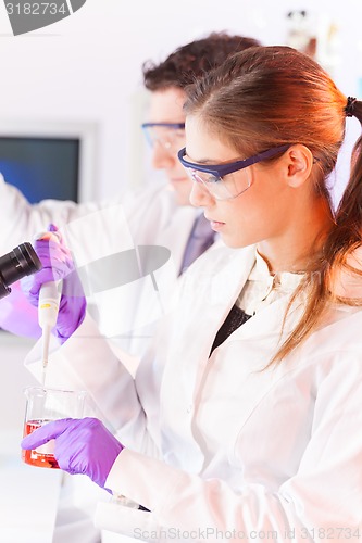 Image of Young scientist pipetting red solution.