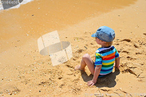 Image of Little toddler boy sitting back on sandy beach