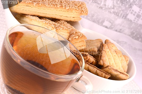 Image of cup of tea and some cookies on white material background