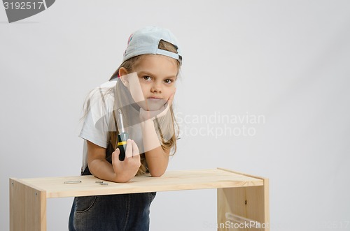 Image of Girl-collector of furniture with a screwdriver wearily leaned on the cabinet