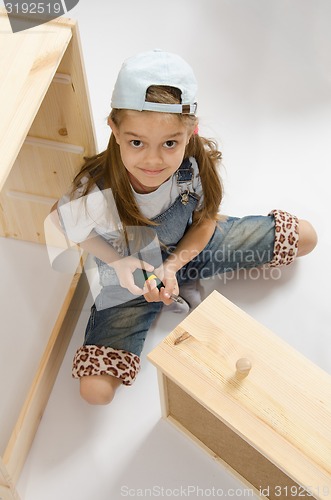 Image of Little girl in overalls collector furniture spins screwdriver
