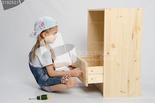 Image of Girl in overalls furniture collector tries to insert drawer a chest of drawers