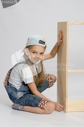 Image of Little girl in overalls collector of furniture turn screw on dresser