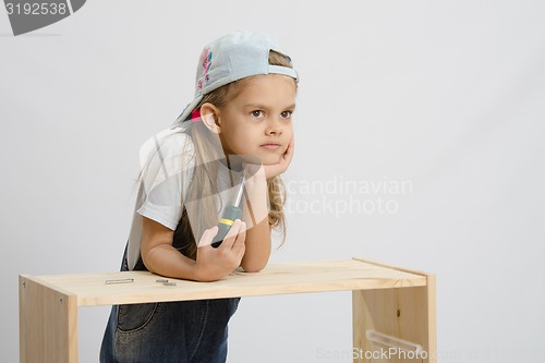 Image of Girl-collector of furniture with a screwdriver thoughtfully leaned her head