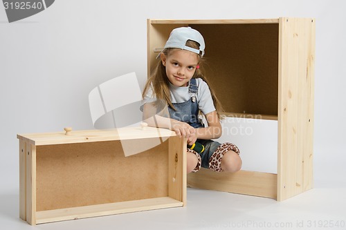 Image of Little girl in overalls sits beside the garbage furniture elements Chest