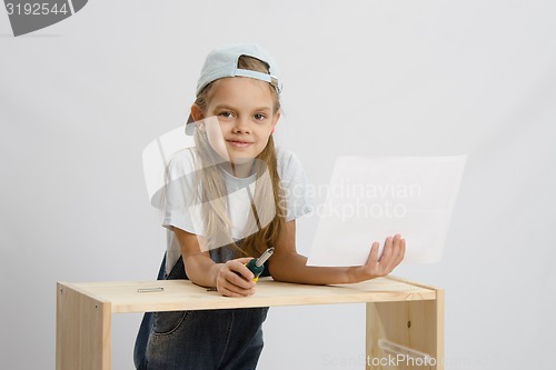 Image of Girl-collector of furniture with a screwdriver and drawing collects furniture