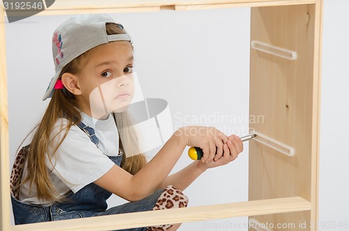 Image of Girl-collector of furniture with a screwdriver collects wooden cabinet