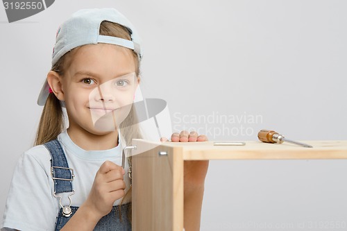 Image of Girl in overalls furniture collector tries to tighten the screw